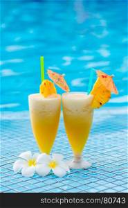 two glasses of cocktail beautifully decorated with pineapple and flowers on the edge of the pool