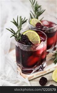 Two glasses of delicious refreshing lemonade with blackberry, ice and lime, decorated of rosemary. Cocktail on light table