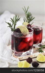 Two glasses of delicious refreshing lemonade with blackberry, ice and lime, decorated of rosemary. Cocktail on light table