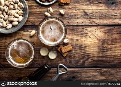 Two glasses of fresh beer and salty snacks on a brown wooden table, top view and space for text