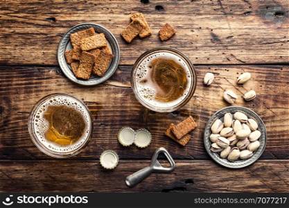 Two glasses of fresh beer and salty snacks on a brown wooden table, top view