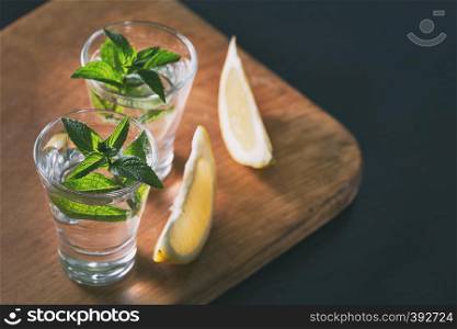 Two glasses of gin or vodka with mint and lemon on wooden background. Alcoholic cocktail. Copy space. Toning.. Two glasses of gin or vodka with mint and lemon on wooden backgr