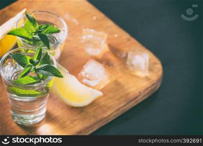 Two glasses of gin or vodka with mint and lemon with ice on a wooden background. Alcoholic cocktail. Copy the space. Two glasses of gin or vodka with mint and lemon with ice