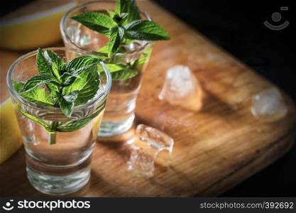 Two glasses of gin or vodka with mint on wooden table with lemon and ice. Alcoholic cocktail. Copy space. Two glasses of gin or vodka with mint on wooden table