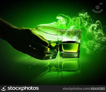Two glasses of green absinth. Hand holding one of two glasses of green absinth with fume going out