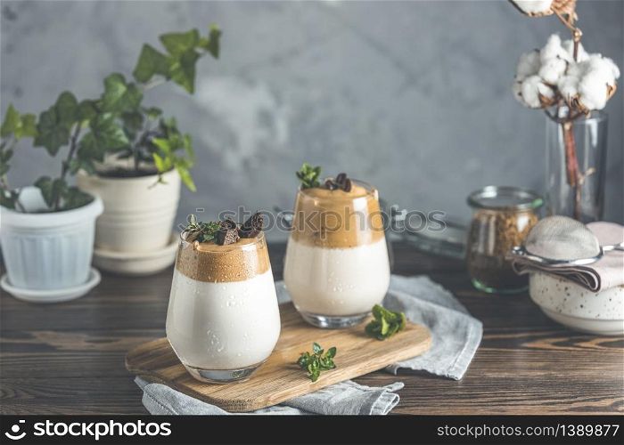 Two glasses of Iced Dalgona Coffee, a trendy fluffy creamy whipped coffee, decorated by thyme and dark chocolate. Ingredients. Dark rustic background, copy space.