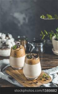 Two glasses of Iced Dalgona Coffee, a trendy fluffy creamy whipped coffee, decorated by thyme and dark chocolate. Dark rustic style.
