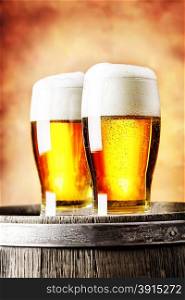 Two glasses of light beer standing on a wooden barrel on a red background. Two glasses of light beer standing on a wooden barrel