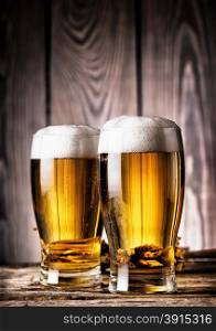 Two glasses of light beer with foam on a wooden background. Two glasses of light beer with foam