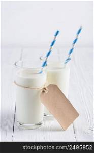 Two glasses of milk with blue stripped paper straw and blank paper tag on rope on white wooden table