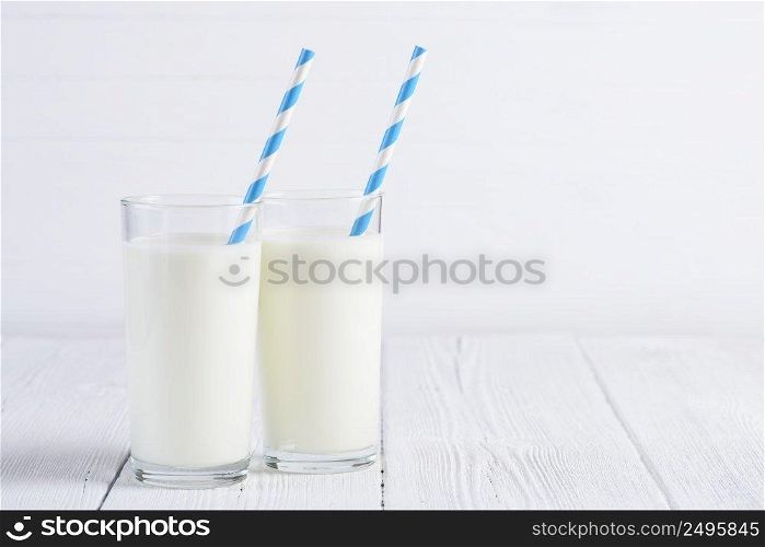 Two glasses of milk with blue stripped paper straw on white wooden table still life