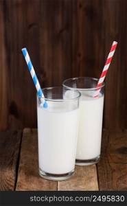 Two glasses of milk with paper straws on vintage wooden table background