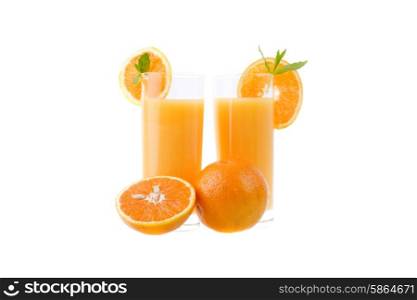 two glasses of orange juice with some oranges