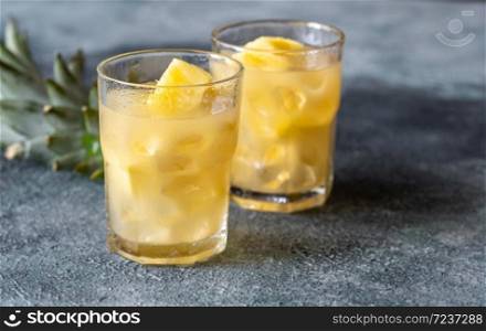 Two glasses of pineapple juice with pieces of fresh fruit