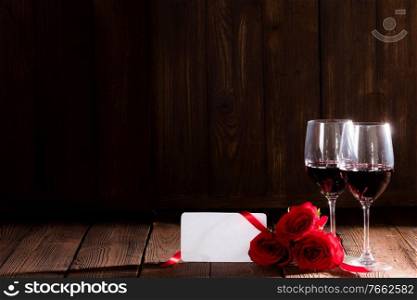 Two glasses of red wine , red roses and blank greeting card on dark wooden background romantic date Valentine day. Wine roses and card