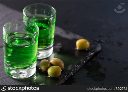 Two glasses of strong absinthe and green olives on a black background. Two glasses of strong absinthe and green olives