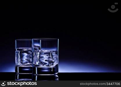 Two glasses of vodka with ice cubes against the background of deep blue glow.