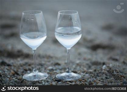 Two glasses of water on the beach. Two glasses of fresh water standing on the sand with pebble. Drinks and refreshment