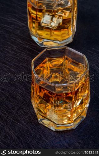 Two glasses of whiskey with ice on a black background. View from above. Two glasses of whiskey with ice on a black background