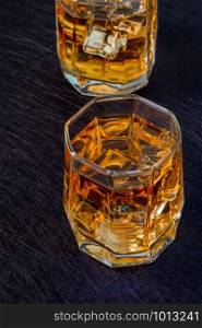 Two glasses of whiskey with ice on a black background. View from above. Two glasses of whiskey with ice on a black background