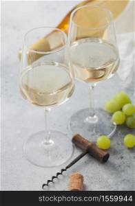 Two glasses of white homemade summer refreshing wine with grapes and corkscrew and bottle on light table background.