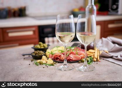 Two glasses of white wine with Italian antipasto meat platter on background.. Two glasses of white wine with Italian antipasto meat platter on background