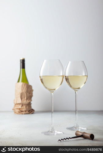 Two glasses of white wine with opener and bottle on light board.