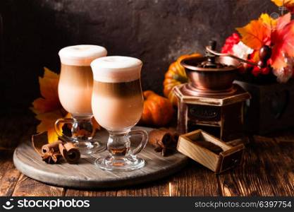 Two glasses pumpkin spicy latte with whipped cream and cinnamon on a wooden stand. Delicious pumpkin spicy latte