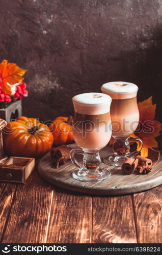 Two glasses pumpkin spicy latte with whipped cream and cinnamon on a wooden stand. Delicious pumpkin spicy latte