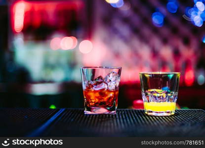 two glasses with cocktails on a rack of bar in night club with bright bokeh. two glasses with cocktails on a rack of bar in night club