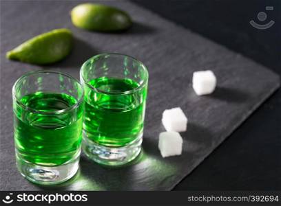 Two glasses with green absinthe lime and sugar on a dark background. Two glasses with green absinthe lime and sugar