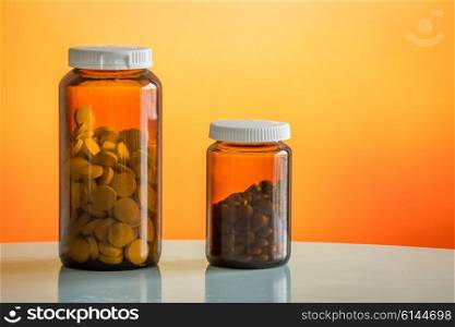 Two glasses with pills on a table on orange background