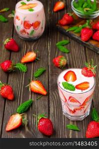Two glasses with strawberry cocktail on a vintage wooden background. Strawberries and spruce tips, ingredients for making smoothies are laid out on the table. Smoothie top view with copy space.