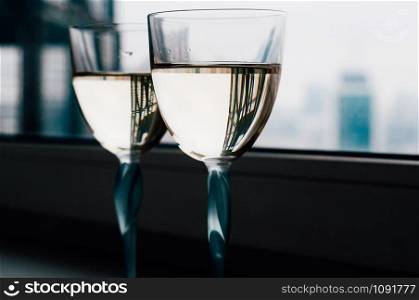 Two glasses with white wine with urban reflections standing on a window sill