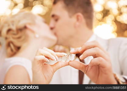 Two gold wedding rings on arms of kissing newlyweds. Small depth of field.