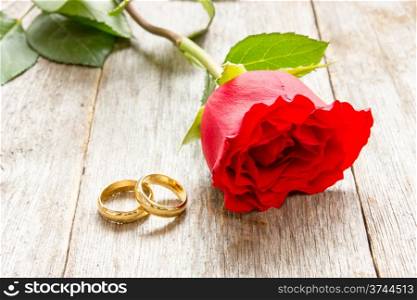 Two golden rings and red rose on old wood background