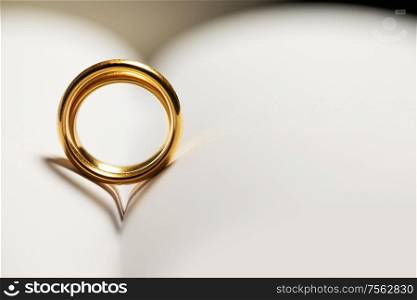 Two golden wedding rings on blank book pages background with copy space for text. Golden wedding rings on book
