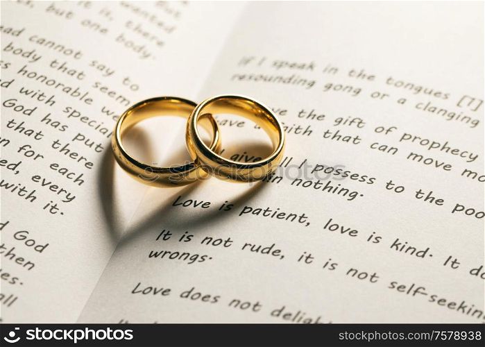 Two golden wedding rings on Holy bible book with heart shaped shadow close up. Golden wedding rings on bible book