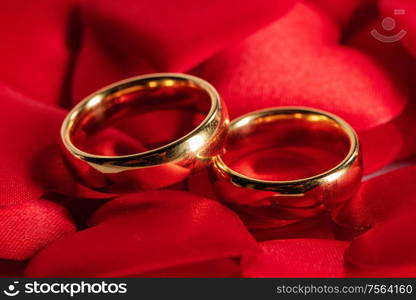 Two golden wedding rings on red satin hearts background. Golden wedding rings on red