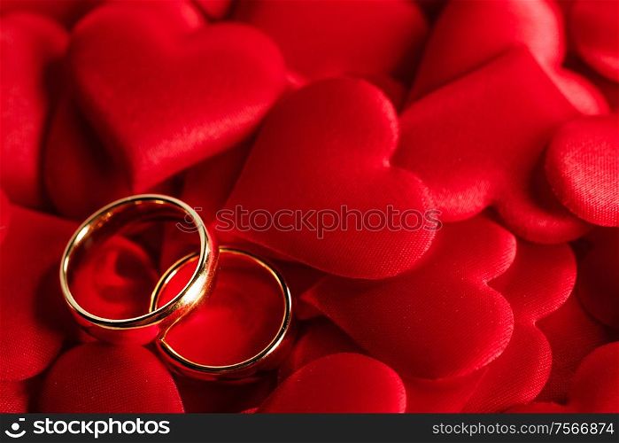 Two golden wedding rings on red satin hearts background. Golden wedding rings on red