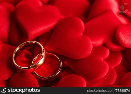 Two golden wedding rings on red satin hearts background. Golden wedding rings on red