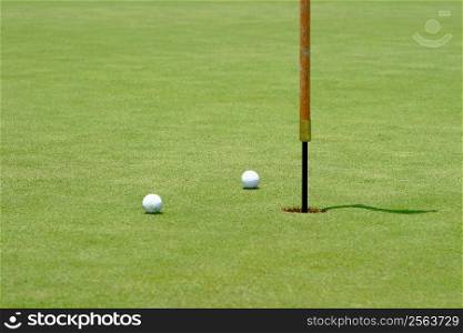 Two golf balls near the flagstick on the green.