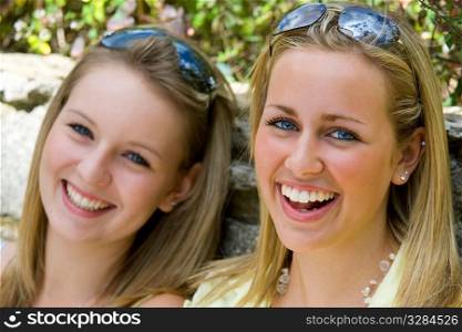 Two gorgeous young blond women laughing and illuminated by summer sunshine.