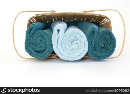 Two green and one teal towel rolled up inside a basket lying over isolated over a white background.