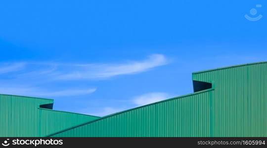 Two green corrugated metal curved roofs of modern industrial warehouse buildings against blue sky background in minimal style