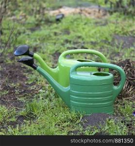 two green watering cans on wet soil of garden