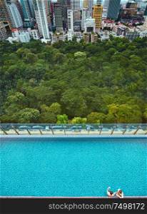 Two guy relaxing in the pool with urban city and green view . View from above .