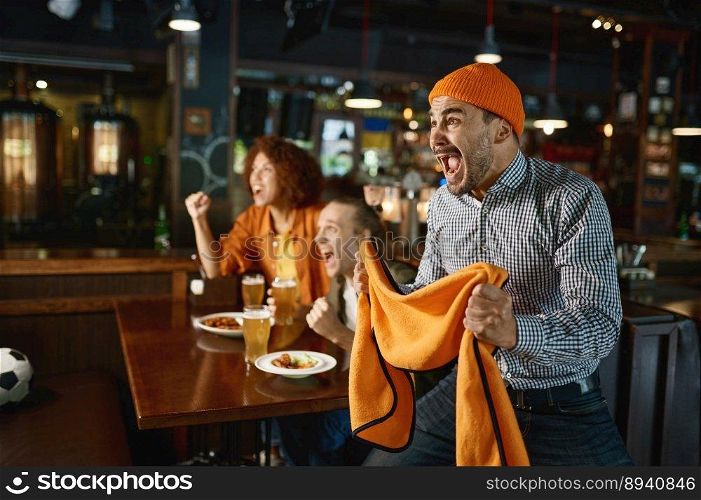 Two guys and woman at pub watching football game and drinking beer. Young excited overjoyed people shouting feeling crazy. Focus on mad man gesticulating with scarf in hands and screaming. Two guys and woman at pub watching football game and drinking beer