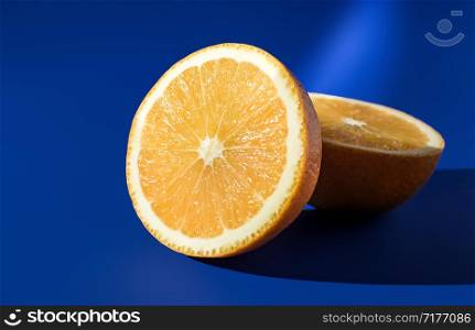 Two halves of ripe orange on a blue background in bright sunlight .. Two halves of ripe orange on a blue background in bright sunlight