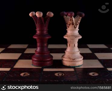 Two hand-decorated, wooden, chess queens are standing on a chessboard.. Two hand-decorated, wooden, chess queens